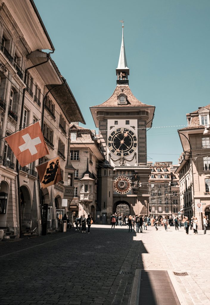 pexels-photo-2399391-2399391 View of Bern's iconic Zytglogge clock tower with Swiss flags and tourists.